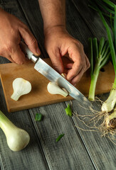 Hands skillfully chop scallions on a cutting board, surrounded by fresh vegetables. The bright...