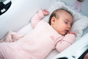 A baby is soundly asleep in a stroller, dressed in a pink onesie, with a soft blanket nearby. The...