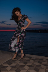 Woman in dress posing standing at pier near sea at the evening
