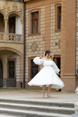 A bride in a lush white dress and veil dancing on the background and historical castle with ancient...