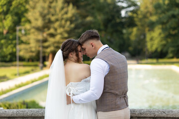 Tender wedding photo of the newlywed to the waist on the background of a park and a...