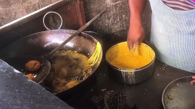 A man making vadapav by picking batata vada dip in besan batter and putting in frying pan with boiling oil. Vadapaav is famous indian dish which mostly pupular in mumbai maharashtra.