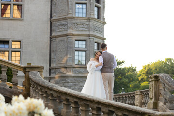 Stylish exterior of a historic castle with newlyweds standing on the steps. Bride resting her head...