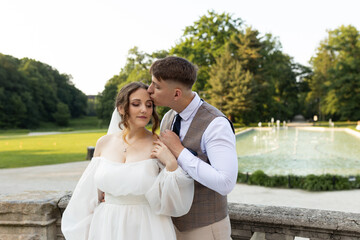 Groom kissing bride on forehead against the backdrop of summer green park with lush green nature....