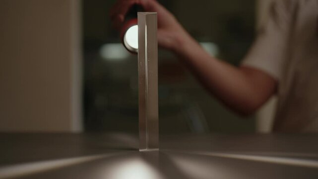 Scientist directing beam of light at triangular glass prism, causing light to refract and split into spectral components, demonstrating principles of optics and physics, close-up, slow motion.