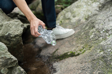Individual Picking Up Plastic Bottle from Rocks. Volunteer actively engaging in environmental...