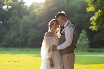 Photos of newlyweds on the background of green trees and warm sunlight. The groom's forehead stuck...