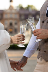 Two wedding glasses with engraving in the hands of the newlyweds against the background of the castle. Crystal champagne glasses in the hands of a couple in love.