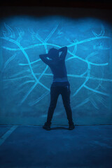 Shadowy figure stands against blue wall, arms raised, creating striking silhouette. background features abstract lines, enhancing mysterious atmosphere of scene