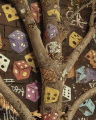 Graffiti art featuring colorful dice brick wall, intertwined with tree trunk, creates vibrant urban scene. playful design adds unique touch to natural setting, evoking creativity and spontaneity