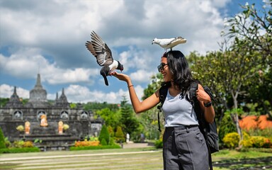 Young Asian woman laughing as a bird lands on her head and another on her hand, in front of a Balinese temple. A joyful and spontaneous travel moment full of fun and connection with nature.
