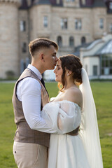Naklejka premium The groom kisses the bride on the forehead and hugs her waist. An incredibly tender wedding photo against the backdrop of the Moszna Castle. A harmonious couple of newlyweds.