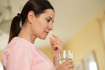 Side profile of a woman about to take a pill with a glass of water, looking thoughtful and focused