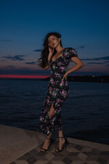 Woman in dress posing standing at pier near sea at the evening