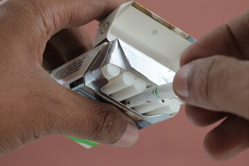 A close-up of a male hand holding a cigarette pack partially pulled out. isolated background.