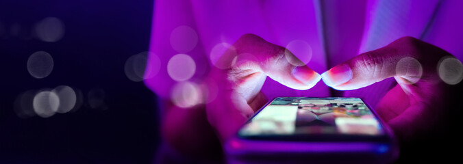 Finger of woman touching scroll page app on mobile phone.In a room with blue and purple neon tones.concept Social media and marketing