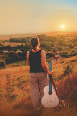 Girl on a mountainside at sunset with a white guitar
