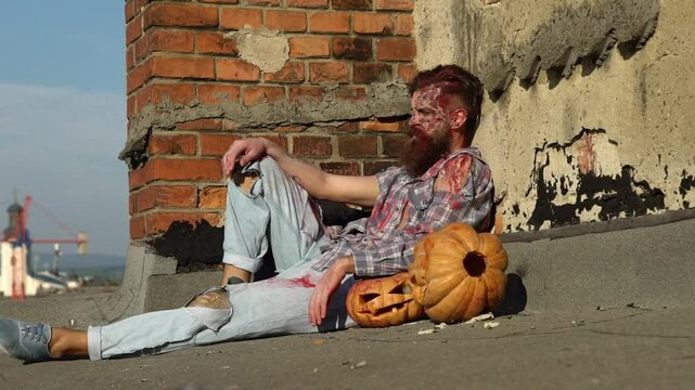 Halloween. Zombie man with Halloween pumpkin. Creepy man with bloody scars Halloween close up face. Man zombie with blood on face. Creative art make-up for Halloween. Man Scary zombie.