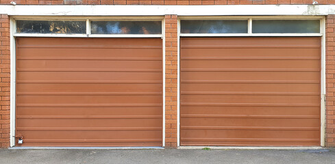 two brown metal garage doors with horizontal lines and glass panels on top against brick wall on building in Sydney, Australia
