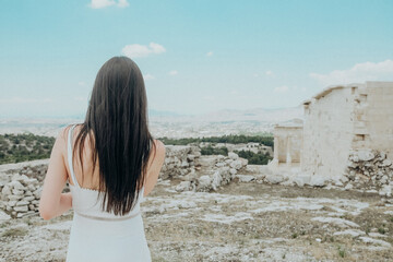 Woman in white dress enjoying the ancient ruins of Acropolis overlooking Athens city