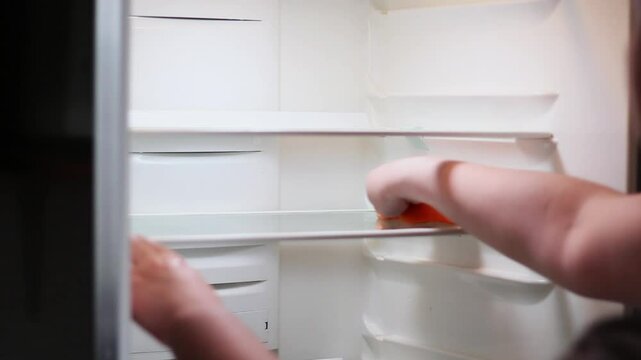 Woman cleaning refrigerator interior with cloth, wiping shelves.