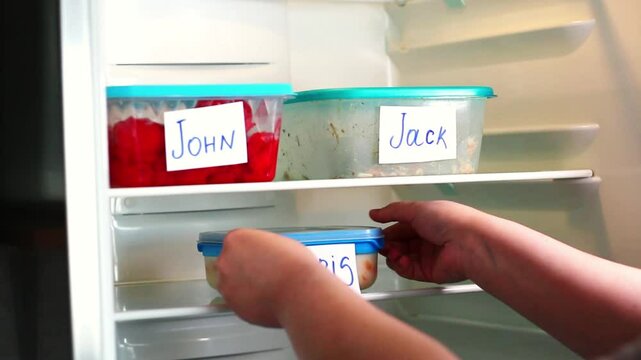 Human putting lunch box in office refrigerator. Office lunch containers with handwritten name stickres. Healthy food preparation for work.