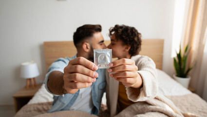 Couple holding condom, kissing on bed, safe sex