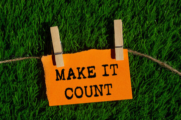 Make it count message written on ripped torn orange paper piece on green grass background....