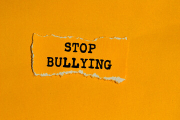 Stop bullying message written on ripped torn orange paper piece on orange background. Conceptual stop bullying symbol. Copy space.