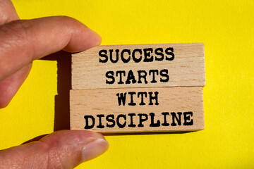 Success starts with discipline message written on wooden blocks on yellow background. Conceptual...