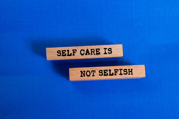 Self care is not selfish message written on wooden blocks on blue background. Conceptual together...