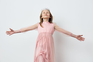 Young girl in a light pink dress with sheer sleeves, wearing a crown, expressing joy and freedom...