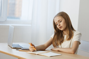 Fototapeta premium Thoughtful young girl writing in a notebook at a light filled study desk, showcasing creativity and focus with a minimalist aesthetic