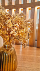 Bouquet of dried yellow wheat ripe crop with seeds in vase of golden colour on brown wooden table...