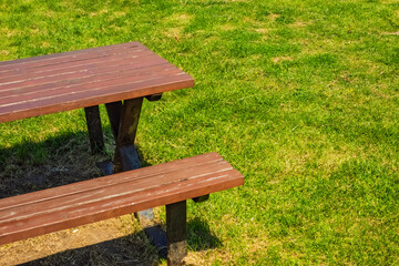Fototapeta premium A simple wooden picnic table with benches is placed on vibrant green grass under bright sunlight. Captured from an angled top view.