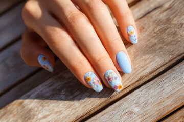 Beautifully manicured nails with floral designs on a sunny wooden table in a cozy outdoor setting