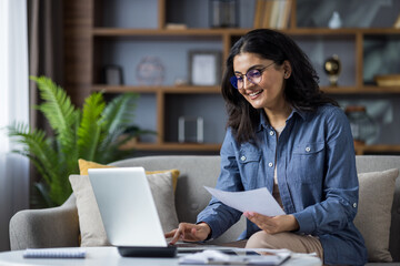 A young Indian woman is sitting at home and working remotely on a laptop and documents