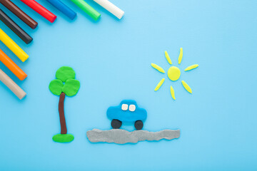 Created car, road, tree and sun from colorful modeling clay on light blue table background. Pastel color. Closeup. Top down view.