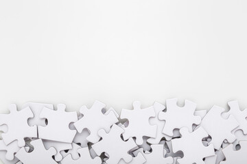Different many white puzzle pieces on light gray table background. Closeup. Empty place for text....