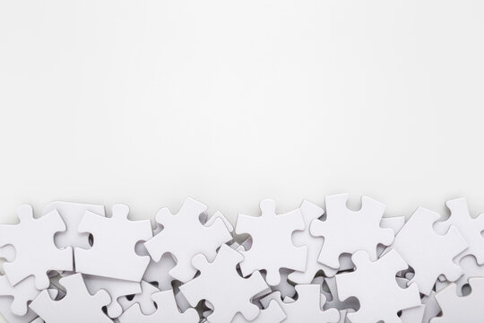 Different many white puzzle pieces on light gray table background. Closeup. Empty place for text. Top down view.