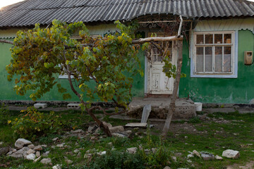 A weathered, traditional rural house with a vibrant green facade and a corrugated metal roof stands...