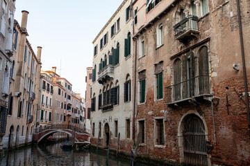 A quintessential view of Burano, Italy, featuring a narrow canal lined with vibrantly colored houses reflecting in the calm water, and traditional fishing boats moored alongside, showcasing the island