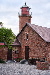 A beautifully picturesque brick lighthouse situated right next to a charming rustic home, all set against a cloudy sky