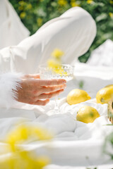 Elegant hand holding a glass near fresh lemons and vibrant flowers in a serene setting