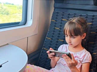 little girl plyas with phone while traveling by train
