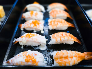 Shrimp sushi nigiri arranged on a black tray, some topped with creamy mayonnaise sauce and orange roe, showcasing traditional Japanese seafood cuisine in high detail.