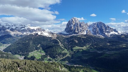 Drone photo of a spiky mountain with snow, forest in the foreground, sky and clouds in the background. shot in 4K in the dolomites, italy
