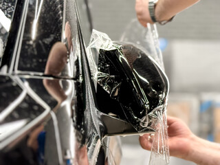 The process of installing PPF on the side of the car. PPF is a polyurethane, protective film that protects the paint from scratches and gravel. Car wrapping close-up. Armored film on the car mirror.