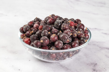 Frozen black currant berries on table in transparent bowl, on light background. Preservation of vegetables and fruits. Natural products