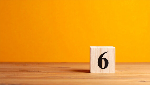 Wooden cube with number 6 on wooden table with orange wall on background.